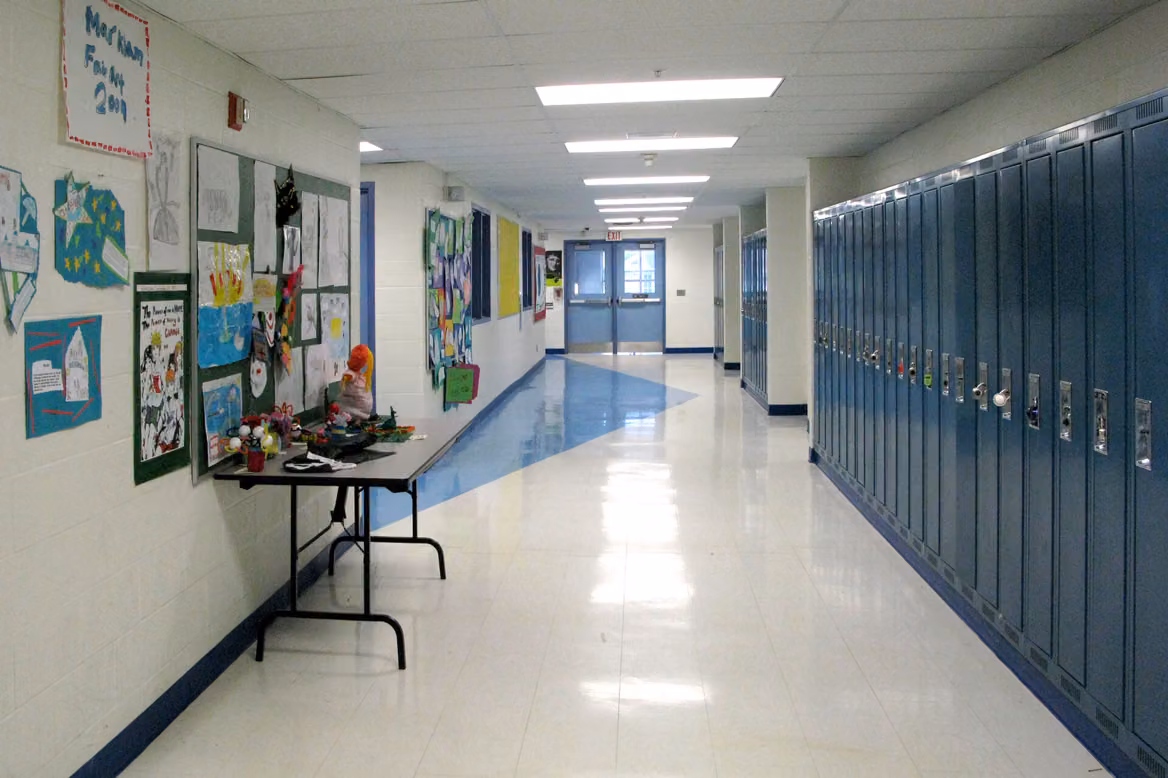 An empty school hallway with a row of blue lockers on one side and student artwork on the other wall.